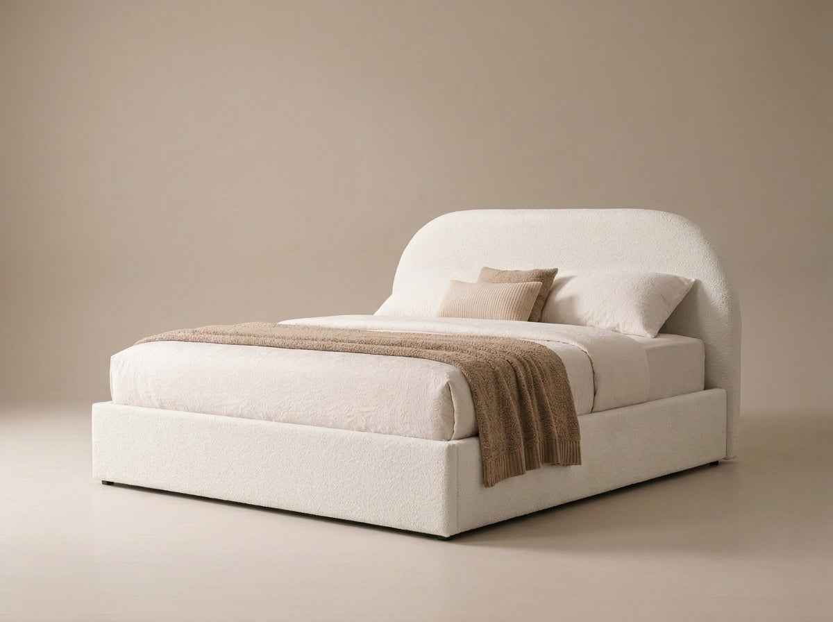 Velets Flora boucle upholstered bed with arched headboard, layered bedding and brown throw.